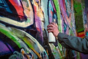 cropped view of street artist painting graffiti with aerosol paint on wall at night